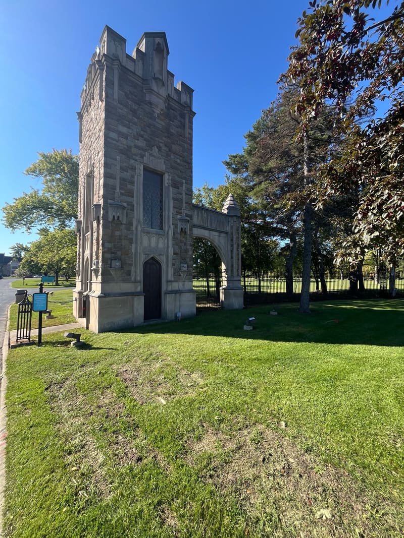 A stone gate tower with battlements and an archway, beside a lawn.