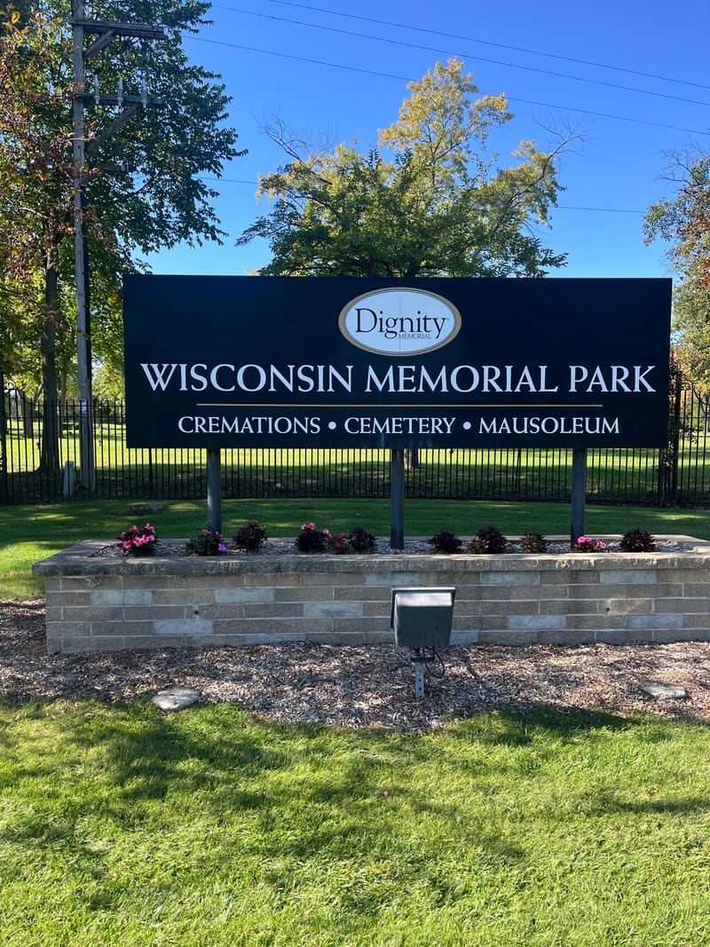The Wisconsin Memorial Park entrance sign above a stone planter with flowers.